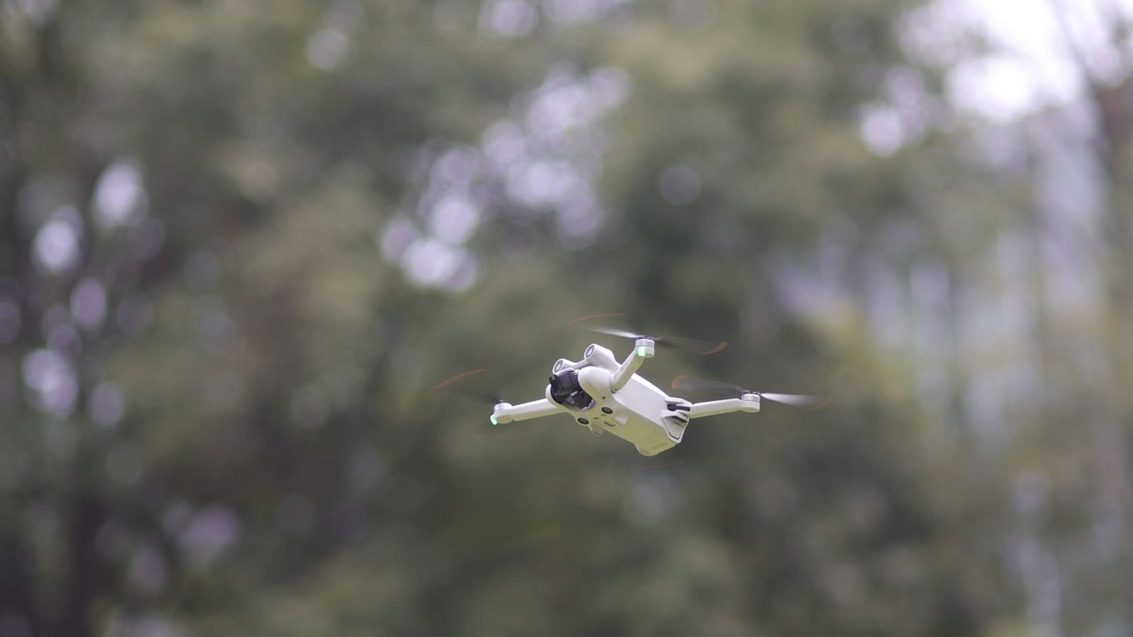 A white quadcopter drone flying against blurred green trees, illustrating Part 108 BVLOS operations